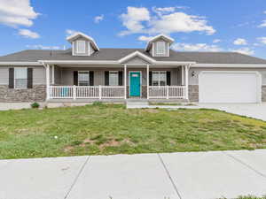 View of front of property featuring covered porch, stone siding, driveway, a garage, and a front lawn