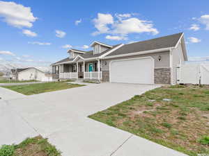 View of front facade featuring a porch, a garage, concrete driveway, and stone siding