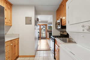 Kitchen with stacked washer / dryer, stainless steel appliances, light countertops, electric panel, and light tile patterned floors