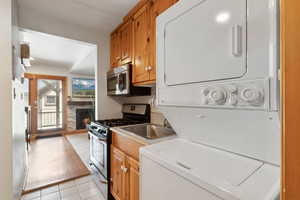 Kitchen with stainless steel appliances, stacked washing machine and dryer, a fireplace, light tile patterned floors, and brown cabinets