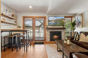 Living room featuring wood finished floors, a stone fireplace, a dry bar, and recessed lighting
