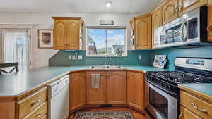 Kitchen featuring appliances with stainless steel finishes, a sink, a peninsula, light wood-style floors, and light countertops