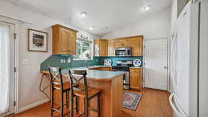 Kitchen featuring stainless steel appliances, a sink, a breakfast bar area, a peninsula, and light wood finished floors