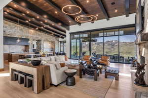 Living room with light wood finished floors, a stone fireplace, a wooden ceiling with exposed beams, and high vaulted ceiling