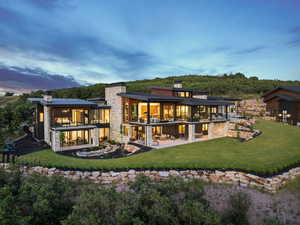Back of house at dusk featuring a balcony, a chimney, a patio area, and a lawn