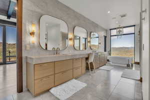 Bathroom with tile walls, a freestanding bath, double vanity, a chandelier, and recessed lighting