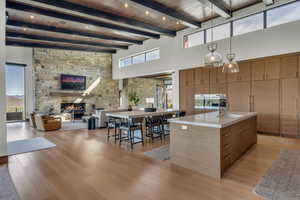 Kitchen with modern cabinets, a center island with sink, a fireplace, hanging light fixtures, and a high ceiling