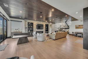 Living room featuring stairway, light wood-type flooring, a stone fireplace, and wooden ceiling