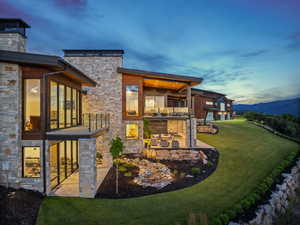 Back of property with a balcony, stone siding, a lawn, a patio, and a mountain view