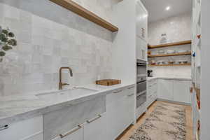 Kitchen with tasteful backsplash, open shelves, light stone counters, and white cabinets