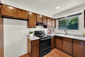 Kitchen with black range with electric cooktop, a sink, under cabinet range hood, light countertops, and light tile patterned floors