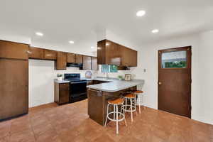 Kitchen featuring black electric range oven, extractor fan, a sink, a peninsula, and a breakfast bar