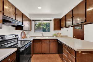 Kitchen featuring electric range, under cabinet range hood, a sink, black dishwasher, and light countertops