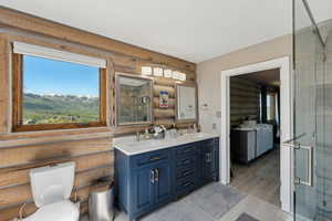 Bathroom featuring log walls, double vanity, a shower with door, and toilet