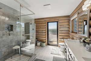 Bathroom featuring log walls, toilet, double vanity, and a shower stall