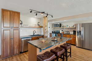 Kitchen featuring appliances with stainless steel finishes, open shelves, a sink, dark countertops, and brown cabinetry