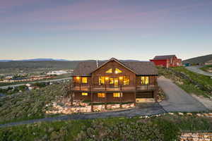 Back of house at dusk featuring a shingled roof, log exterior, and a deck with mountain view