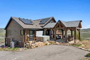 View of front facade featuring roof with shingles, log siding, solar panels, a patio area, and central air condition unit