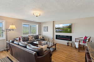 Living room with light wood finished floors, a glass covered fireplace, a textured ceiling, and baseboards