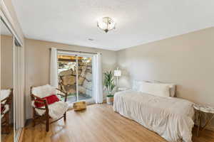 Bedroom featuring access to outside, wood finished floors, a textured ceiling, baseboards, and a closet