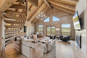Living room featuring wood ceiling with exposed beams, high vaulted ceiling, light wood-style floors, a high end fireplace, and log walls