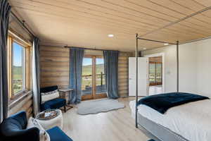 Bedroom with rustic walls, wooden ceiling, multiple windows, access to exterior, and wood finished floors