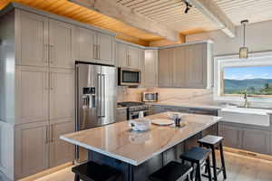 Kitchen featuring high end appliances, wood ceiling with exposed beams, a sink, a breakfast bar area, and light stone counters