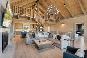 Living area featuring wood walls, stairs, light wood finished floors, high vaulted ceiling, and a premium fireplace