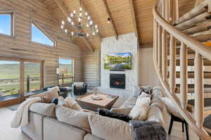 Living area with wooden ceiling with exposed beams, high vaulted ceiling, a chandelier, wood finished floors, and rustic walls