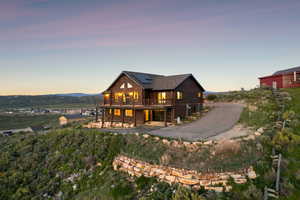 Back of property at dusk featuring a wooden deck, log exterior, solar panels, and roof with shingles
