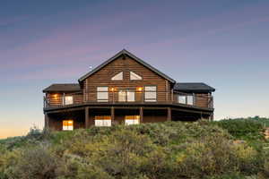 Back of property at dusk with a balcony, log exterior, and roof with shingles
