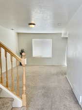 Carpeted spare room featuring stairs, baseboards, a smoke detector, and a textured ceiling
