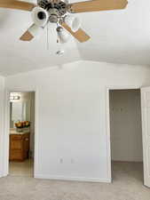 Unfurnished bedroom featuring a spacious closet, light carpet, vaulted ceiling, ensuite bathroom, and ceiling fan