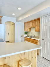 Kitchen featuring white appliances, light countertops, light tile patterned floors, a breakfast bar, and a sink