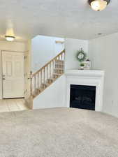 Unfurnished living room with carpet floors, a textured ceiling, stairs, a fireplace, and baseboards