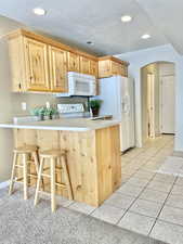 Kitchen featuring white appliances, arched walkways, a peninsula, a breakfast bar area, and light brown cabinets