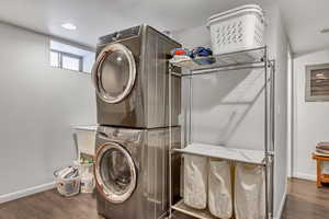Laundry area with stacked washing machine and dryer, baseboards, wood finished floors, and recessed lighting