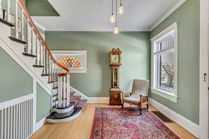 Living area featuring healthy amount of natural light, crown molding, wood finished floors, stairway, and baseboards