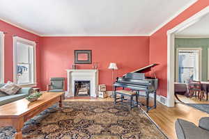 Living room featuring wood finished floors, crown molding, a fireplace with flush hearth, and baseboards