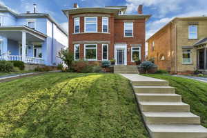 View of front of home featuring a chimney, brick siding, and a front yard