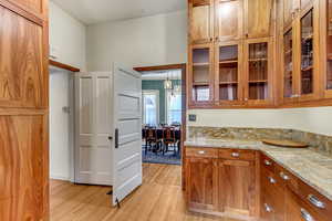 Kitchen featuring light wood-style floors, brown cabinetry, light stone counters, and glass insert cabinets