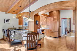 Dining space featuring arched walkways, light wood-type flooring, wooden ceiling, and baseboards