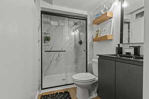 Full bathroom featuring toilet, vanity, a marble finish shower, and wood finished floors