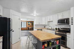 Kitchen with stainless steel appliances, wooden counters, a sink, a textured ceiling, and white cabinets