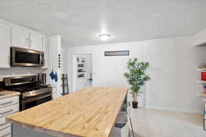 Kitchen with appliances with stainless steel finishes, white cabinetry, a kitchen island, wood counters, and light tile patterned floors