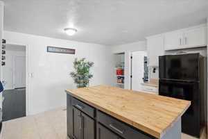 Kitchen with freestanding refrigerator, butcher block counters, white cabinetry, a center island, and baseboards