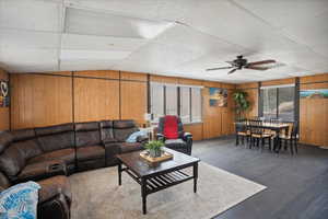 Living area with a paneled ceiling, wood walls, ceiling fan, and wood finished floors