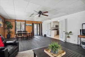 Living room featuring french doors, dark wood finished floors, wooden walls, a ceiling fan, and a paneled ceiling