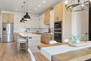 Kitchen with stainless steel appliances, a chandelier, a kitchen island with sink, recessed lighting, and light countertops