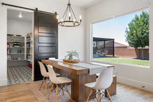 Dining room with a barn door, wood finished floors, a chandelier, and healthy amount of natural light